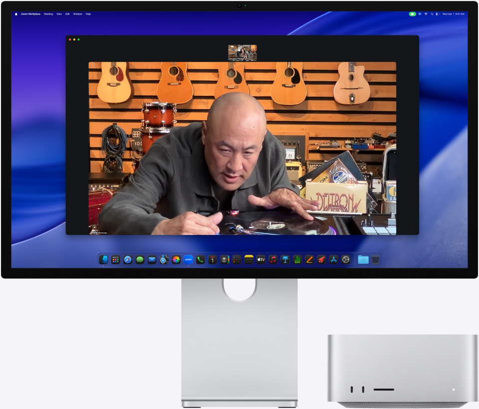 Lors d’un appel vidéo sur un Studio Display XDR avec un Mac Studio glissé en dessous, une personne dans un magasin de musique examine de près une platine