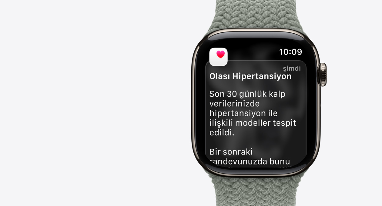Apple Watch Series 11, natürel renk, titanyum kasa, olası hipertansiyon bildirimi, beyaz kutu içinde pembe kalp, sağ dış görünüm, Digital Crown, kordon, yeşil gri renkte Örgü Solo Loop