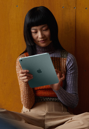 A student sitting on the floor against a wall. She's holding an iPad.