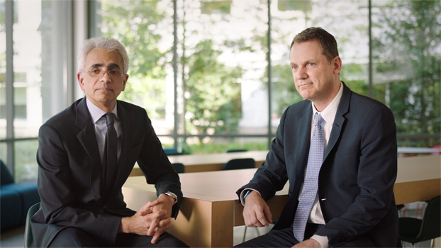 Duas pessoas de terno sentadas à mesa.