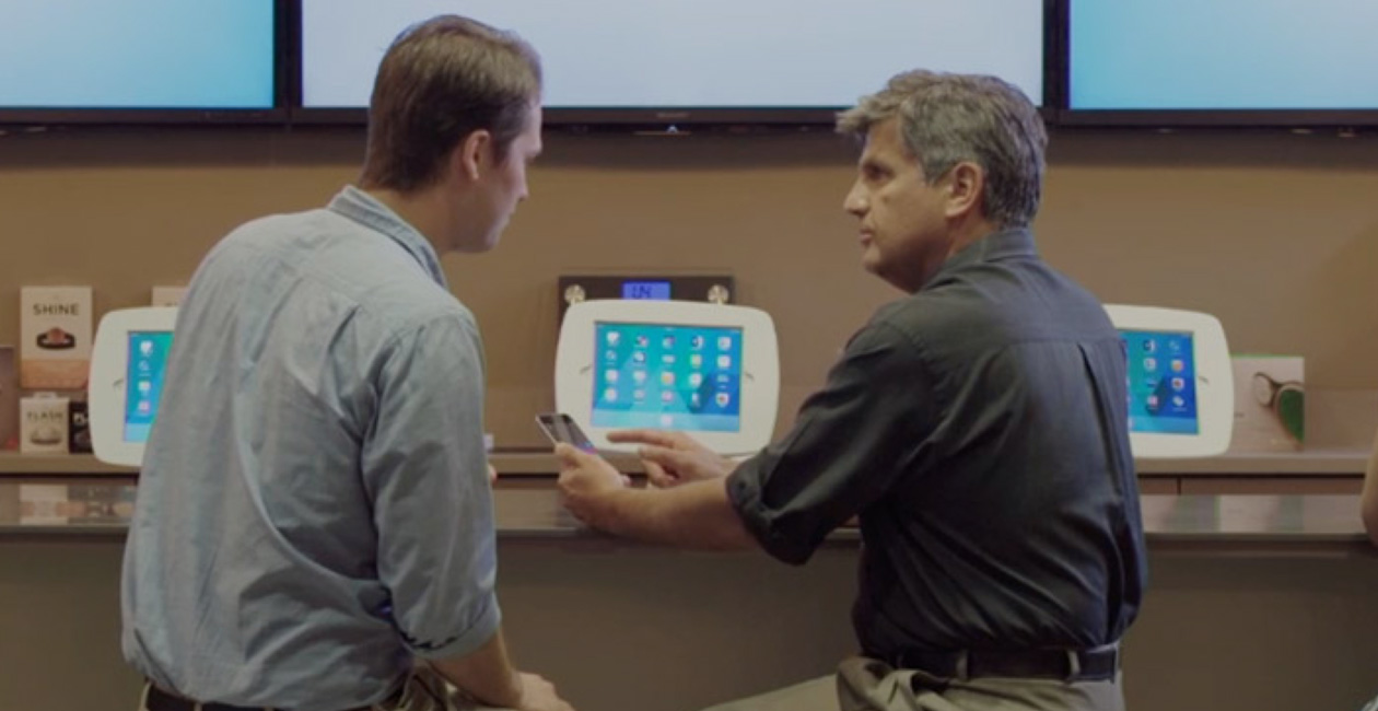 Dois homens sentados no O Bar, olhando para a tela de um iPhone.